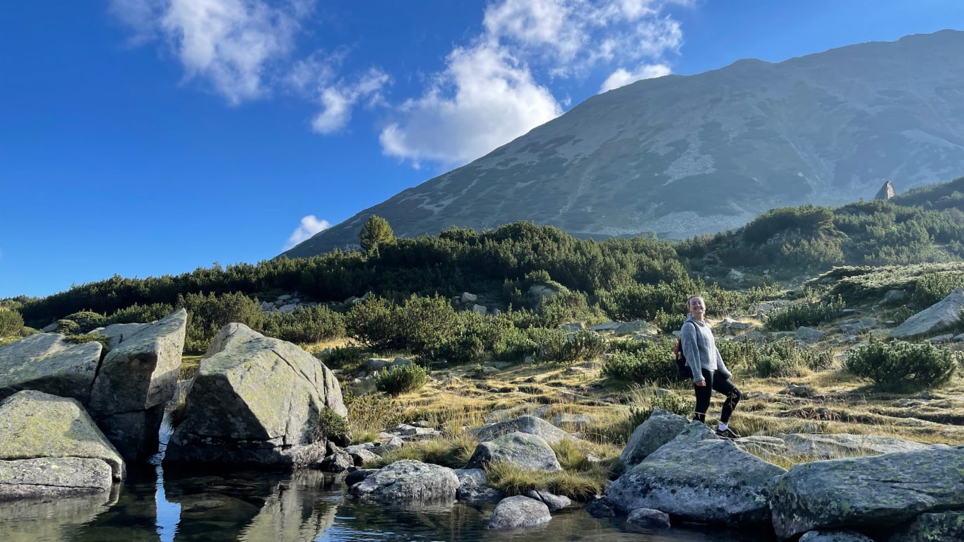 Meg hiking in the pirin mountains, standing at the edge of a stream
