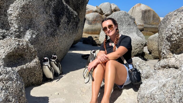 Meg sat ont he white sand beach with boulders and African penguins