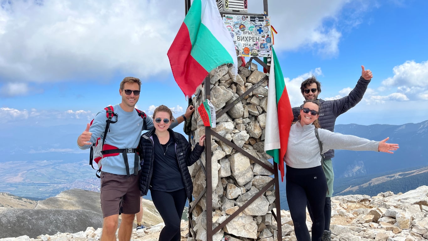 Four friends standing at the top of the peak of Vihren Mountain in Bulgaria